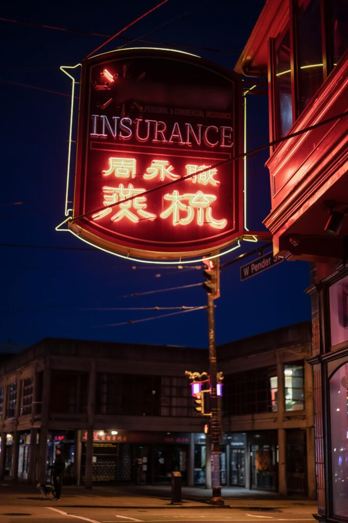 Vibrant neon insurance sign illuminating a city street at night.